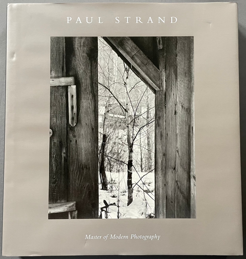 A hardcover art book titled 'Master of Modern Photography' by Paul Strand, featuring a black and white photograph of a rustic wooden doorway looking out onto a snowy winter landscape. The book is photographed flat against a neutral gray background.