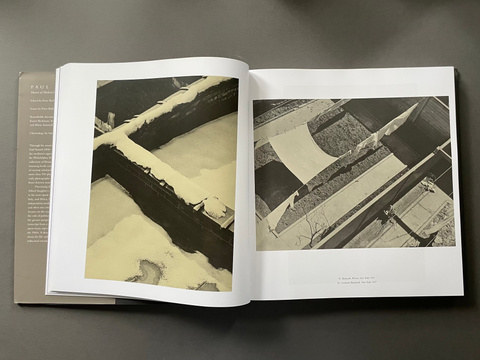An open hardcover book laid flat on a dark gray surface, showing two interior pages with black-and-white architectural photographs and printed text.