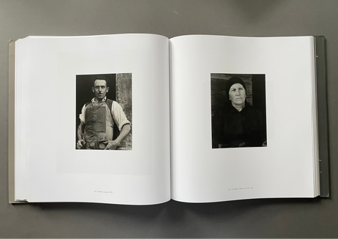An open hardcover book laid flat on a dark gray surface, showing two black-and-white portrait photographs printed on the white pages.