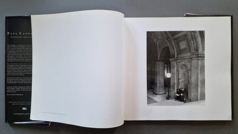 An open book showing a black-and-white architectural photograph on the right page and printed text on the left page, photographed from above on a dark gray surface.