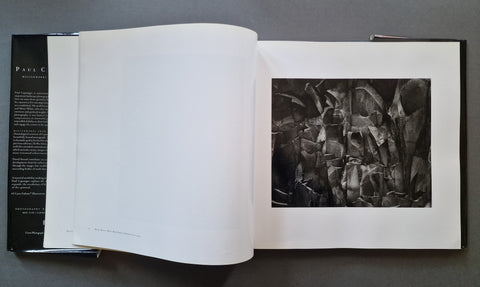 An open art book displayed flat on a dark gray surface, showing a black and white abstract photograph printed on the right page with a white margin and a black text page on the left.