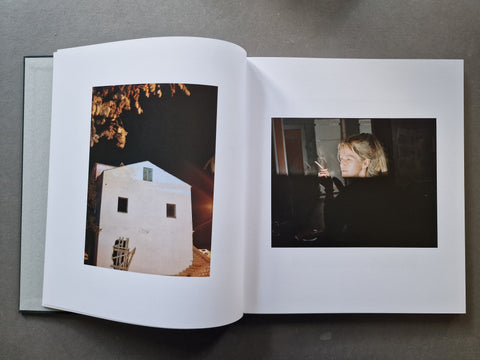 An open book, showing two printed photographs on the pages: one of a white building at night and one of a person in a dark interior.