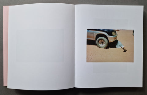 An open book , showing mostly blank white pages with a small inset photograph on the right page depicting part of a vehicle and a person on sand.