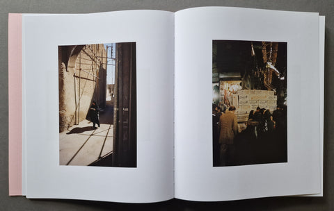 An open book, showing two printed photographs on white pages. The left page contains a warm-toned street scene with a person walking under strong sunlight, and the right page shows a darker nighttime market or street scene with several people.