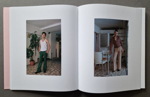 An open book, showing two printed fashion photographs on the left and right pages. The left page photo shows a man in a white tank top and green pants standing indoors; the right page photo shows a woman in a red-and-white check shirt and light pants standing indoors.