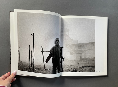 An open book or photo journal displayed against a dark gray background, showing a black-and-white photographic print with a person standing outdoors in a foggy scene.