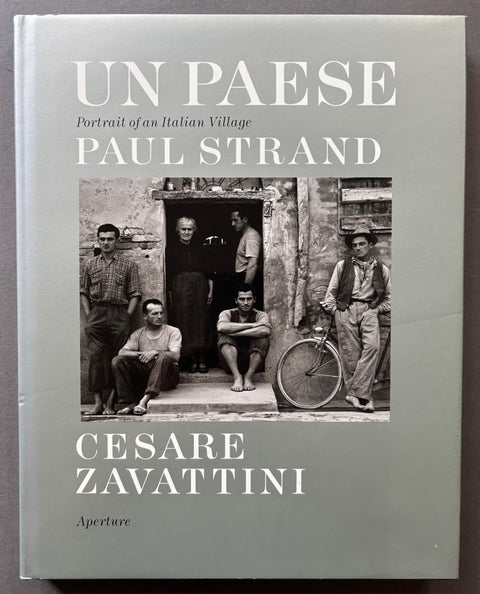 Book titled 'Un Paese: Portrait of an Italian Village with a silver cover and an image featuring a group of Italian men gathered around a doorway.