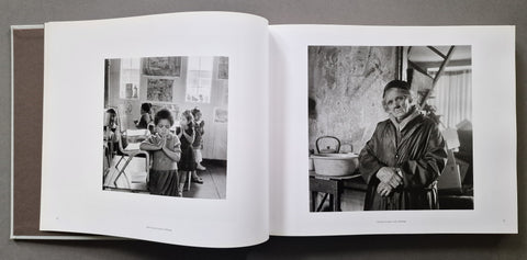 An open book, showing two black-and-white portrait photographs printed on white pages one of a small child and one of an old woman.