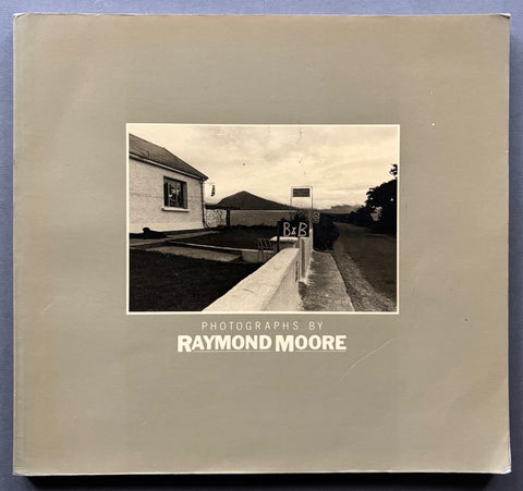 Book titled 'Photographs by Raymond Moore' with a beige cover featuring the image of a B&B sign next to a low wall.