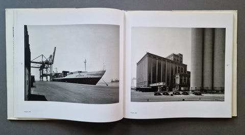 An open book showing two black-and-white photographic prints side by side on white pages, photographed against a dark gray background.