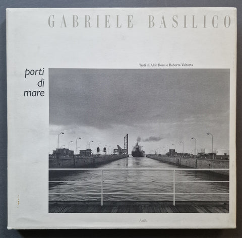 A square book titled 'GABRIELE BASILICO' and 'porti di mare' shown flat against a dark background. The cover features a black-and-white photograph of a canal or port lock with a ship in the distance, plus small text credits and the publisher mark 'Anki' near the bottom.