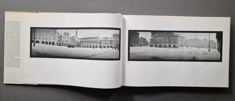 An open book showing two black-and-white panoramic architectural photographs printed on white pages, photographed against a dark gray background.
