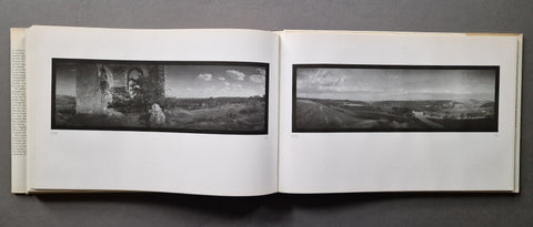 An open book displaying two panoramic black-and-white landscape photographs printed on white pages, photographed against a dark gray background.