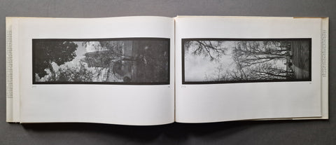 An open book showing two wide black-and-white landscape photographs side by side on white pages, photographed from above against a dark gray background.