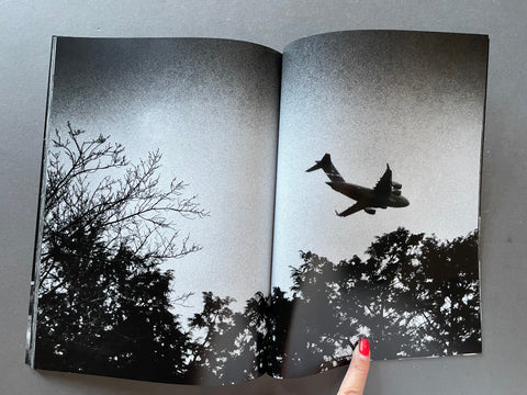 Open book showing a black and white photo of an airplane flying over trees.