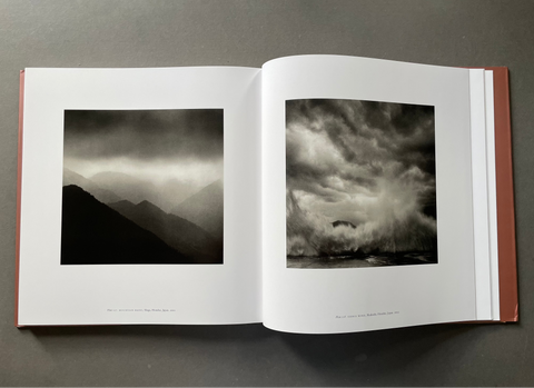 An open hardcover art book lying flat on a dark gray surface, displaying two black and white landscape photographs printed on the pages.