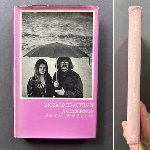 A pink hardcover book titled 'A Confederate General from Big Sur' by Richard Brautigan, shown from the front and spine. The front cover features a black-and-white photograph of a man and woman under a large umbrella.