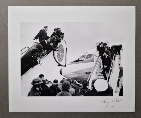 A black and white signed silver gelatin print of The Beatles getting on an airplane, Terry O'Neill's signature in the bottom right corner