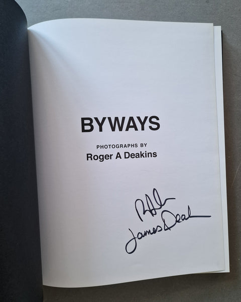 An open book showing a white title page with the text 'BYWAYS', 'PHOTOGRAPHS BY Roger A Deakins', and a black handwritten signature.