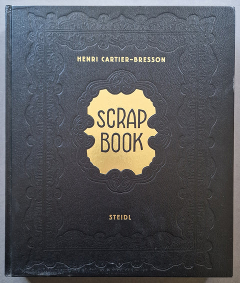 The front cover of the 'Scrap Book' book by Henri Cartier-Bresson, published by Steidl. The cover is a textured black leather-like material with an embossed decorative border, featuring a central gold shield emblem with the title 'SCRAP BOOK' in black text.