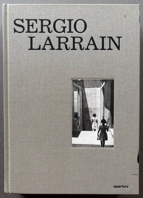 Book titled 'Sergio Larrain' published by Aperture with a grey cloth cover featuring a black and white photograph of a woman walking down stairs followed by a young girl.