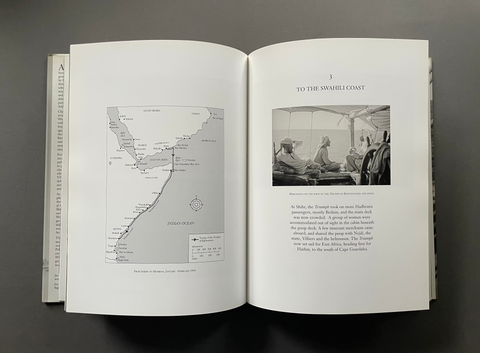 An open book laid flat on a dark gray surface, showing two interior pages with a grayscale map on the left page and a black-and-white photograph with text on the right page.