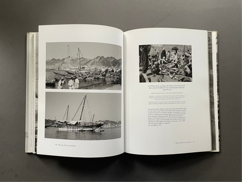 An open book laid flat on a dark gray surface, showing two printed pages with black-and-white photographs and text. The left page contains two scenic harbor and boat photos, and the right page has one larger historical photo above a block of text.