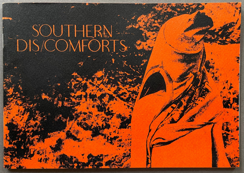 A rectangular printed cover or poster with the text 'SOUTHERN DIS/COMFORTS' in orange on a black-and-orange distressed background, photographed against a gray textured surface.