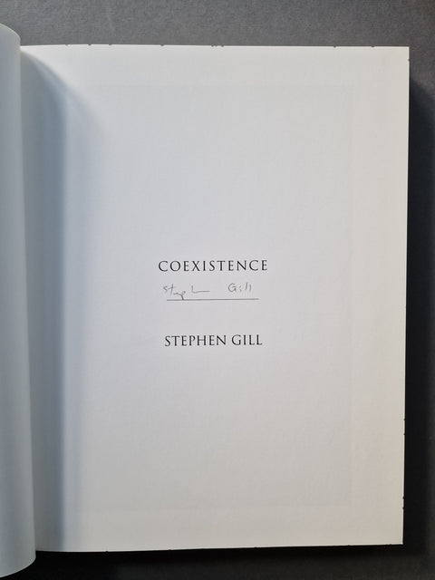 An open book showing a white interior page with the title 'COEXISTENCE', a handwritten signature, and the author name 'STEPHEN GILL' printed in black serif text.