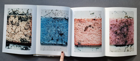 An open art book, showing four printed panels with textured rectangular color samples in black, blue, peach-pink, and dusty rose.