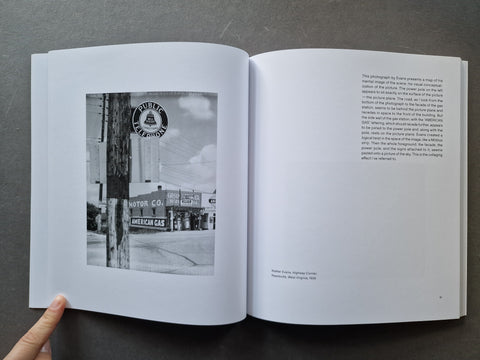 An open book showing a black-and-white photograph of a vintage roadside sign on the left page and printed text on the right page