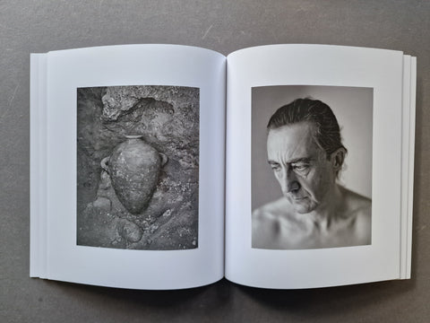 An open book, displaying two black-and-white photographic prints on the pages: a textured stone vessel on the left page and a portrait of a man on the right page.