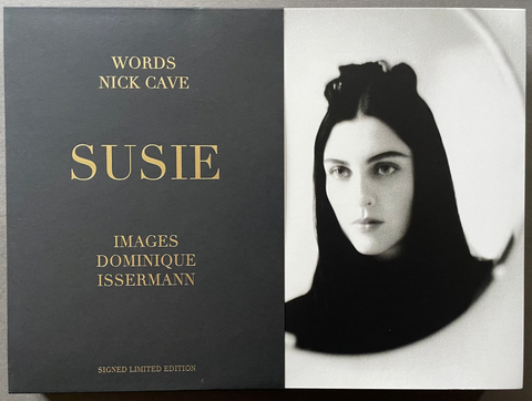 The front cover of the book 'Susie: Words by Nick Cave, Images by Dominique Issemann' is shown. The cover is split vertically: the left half is dark charcoal gray with gold text, and the right half is a black-and-white portrait photograph of a woman.