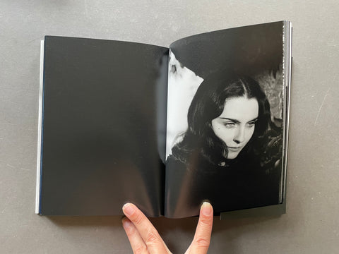 An open hardcover book or photo album laid flat on a gray surface, with a black-and-white photograph of Susie visible on the right page and a hand holding the bottom edge.