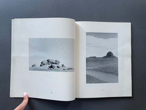 An open book or photo journal laid flat on a dark gray surface, showing two interior pages with black-and-white landscape photographs.