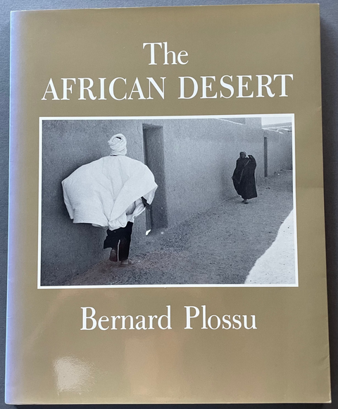 The African Desert book by Bernard Plossu, featuring a beige cover with a central black and white photograph of a desert scene, displayed on a dark gray surface.