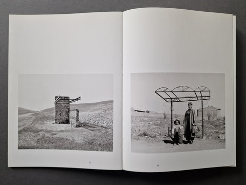 An open book showing two black-and-white photographic prints on the pages, photographed against a dark gray background.