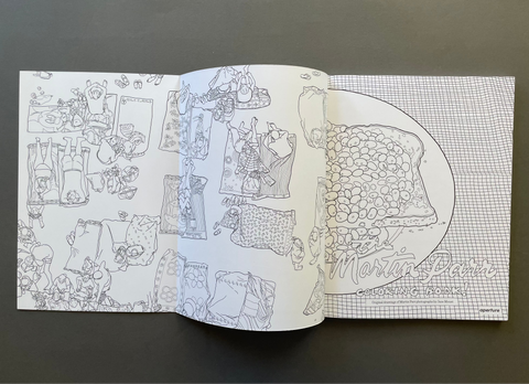 An open coloring book laid flat on a dark gray surface, showing two spread pages with black-and-white line drawings and a grid pattern. One page features multiple small illustrated scenes, and the other shows a large outlined drawing with the title 'Martin Parr' in script.