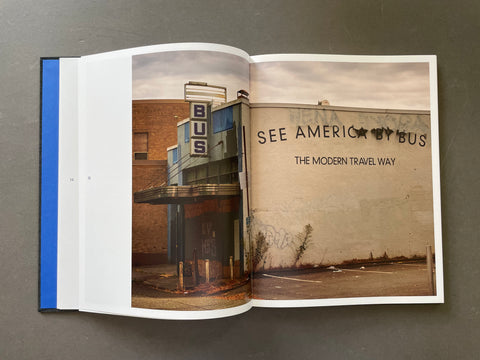An open book or magazine spread lying on a dark gray surface. The pages show a sepia-toned photograph of a building with the text 'BUS' and 'SEE AMERICA BY BUS THE MODERN TRAVEL WAY.