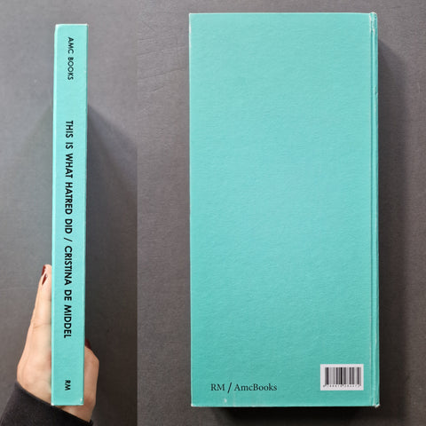 A mint turquoise hardcover book shown upright, with the spine visible on the left and the back cover visible on the right. A hand with red nail polish is holding the spine.