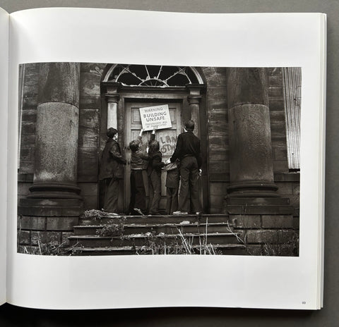 Black and white photograph of a group of people standing on steps in front of a building with signs.