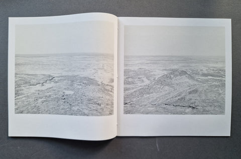 An open book showing two grayscale landscape photographs side by side on a dark gray surface.