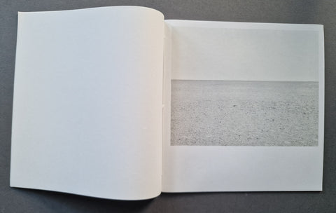 An open book showing a minimalist landscape photograph of a flat, textured gray plain on a white page, set against a dark gray background.