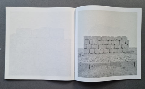 An open book, showing a mostly blank left page and a grayscale photograph of stacked stone blocks on the right page.