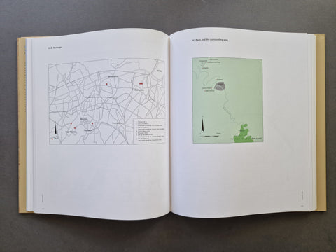 An open book laid flat on a dark gray surface, showing two interior pages with printed maps and labels. The left page contains a detailed street map, and the right page contains a smaller map with a green highlighted area.