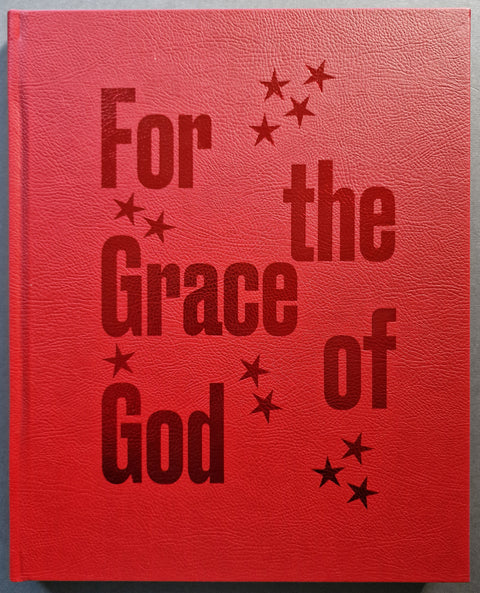 A red textured book with embossed dark red text reading 'For the Grace of God' and small star motifs, shown against a neutral gray background.