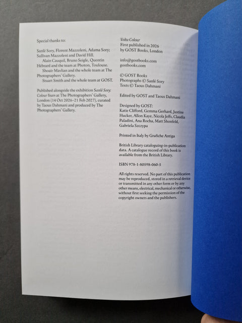 A printed booklet or instruction sheet with black text on white paper, photographed from above against a blue surface with a hand visible at the top right.