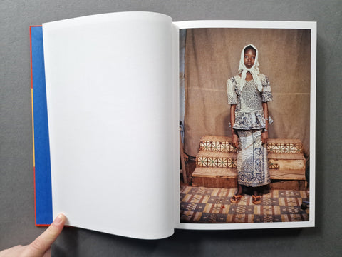 An open book spread with a blank left page and a portrait of a black woman dressed in a matching outfit and a headscarf on the right