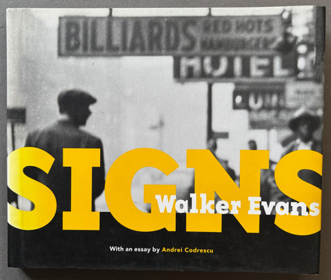 Book titled 'Signs' by Walker Evans with a black cover featuring an image of a man in a street with building signs.
