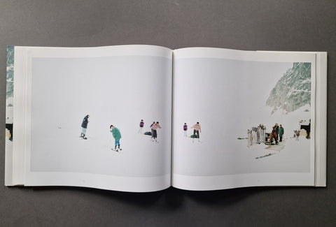 An open art book, showing two printed pages with minimalist winter scenes featuring small figures in a snowy landscape.